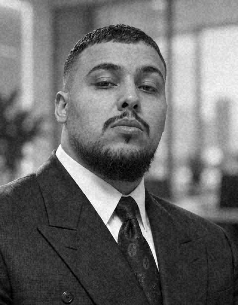 The founder of Recalibre, photographed in black and white in a suit and tie, with an office out of focus behind him.